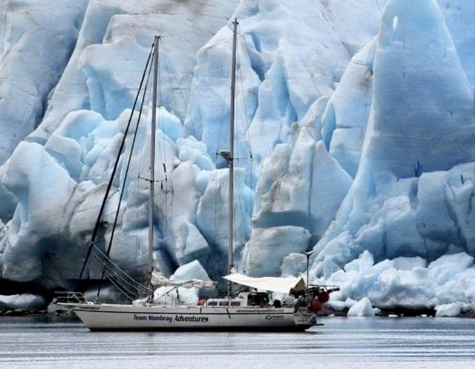 The expedition yacht dwarfed by a wall of blue glacier ice, Antarctic Peninsula