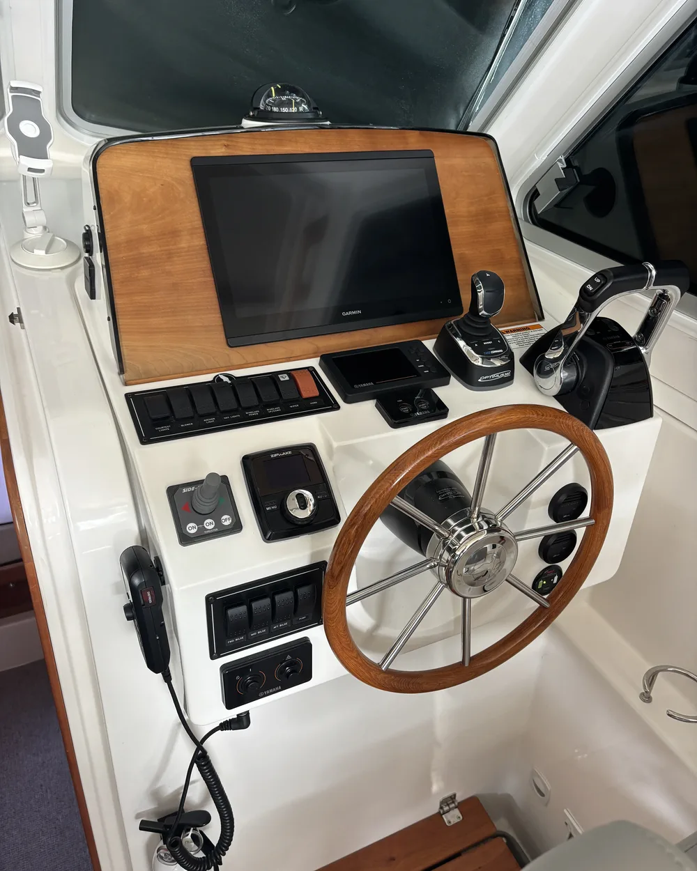 A well-kept helm console: timber wheel, navigation screens and engine controls