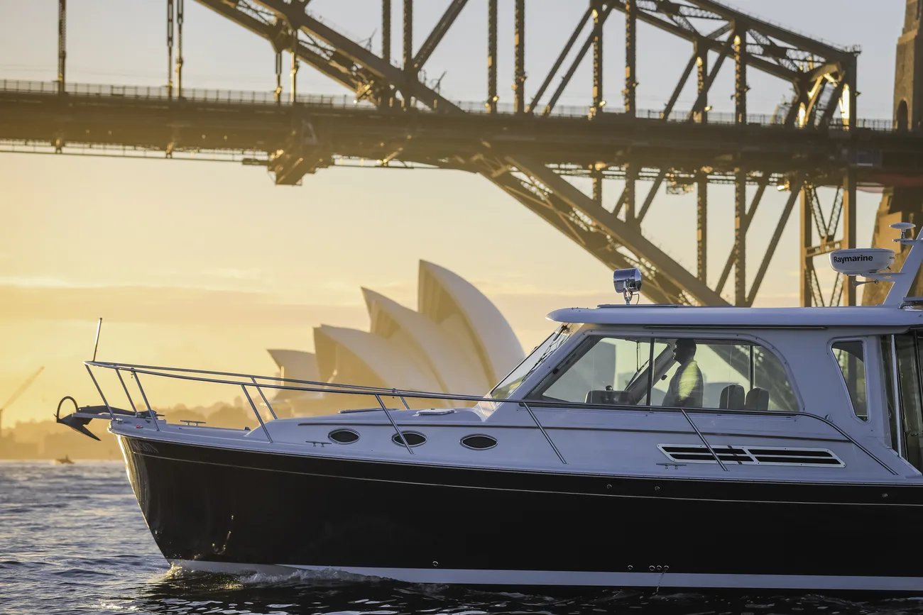 A professional skipper at the helm passing under the Sydney Harbour Bridge at golden hour